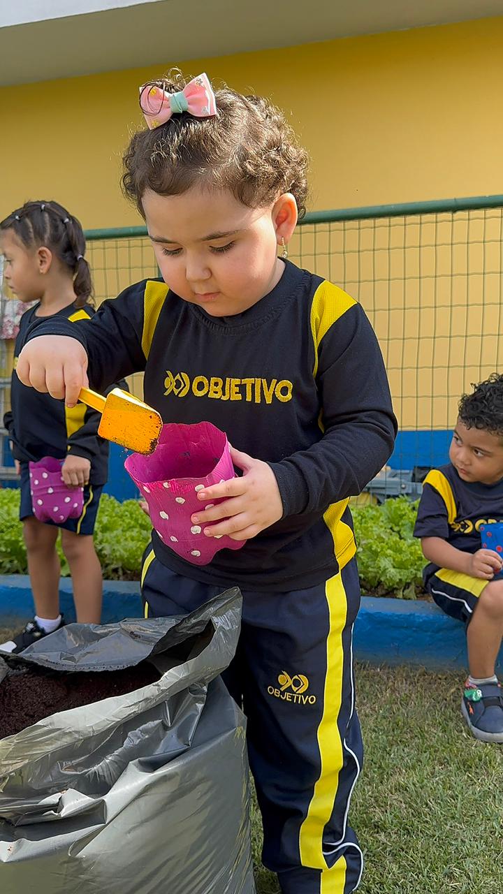 Aluna da Educação Infantil plantando em um vaso na horta da escola