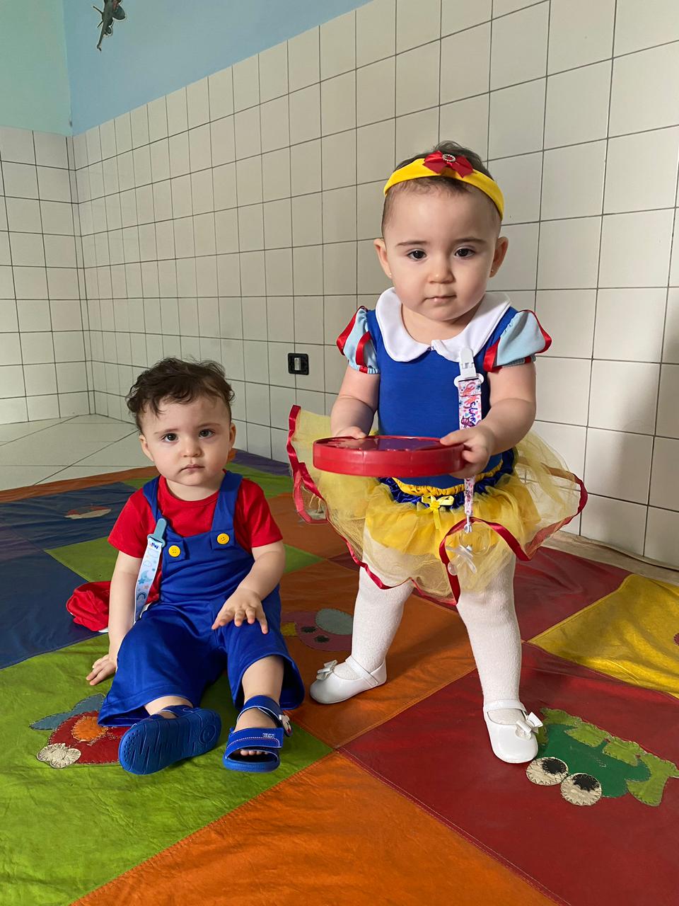 Dois bebês do berçário fantasiados, brincando no tapete da sala